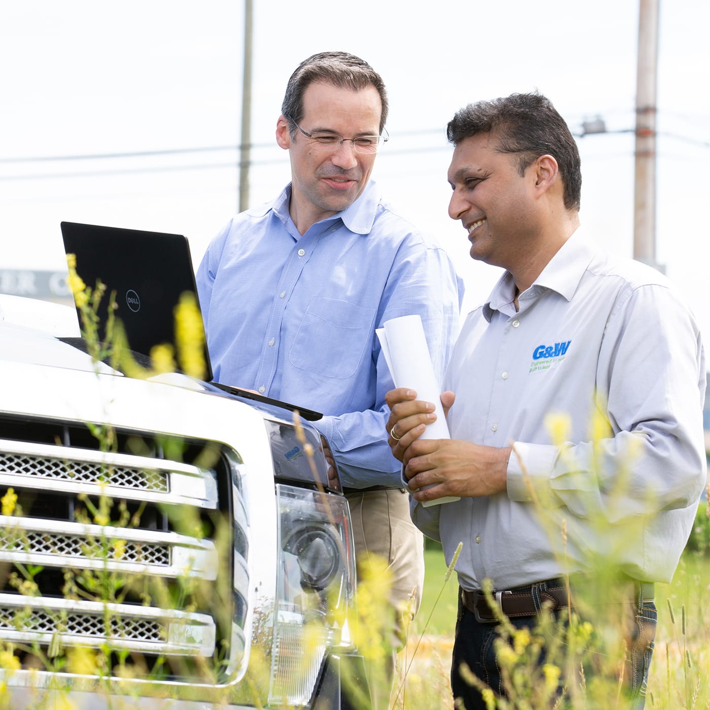 Two men looking at a laptop in a field.